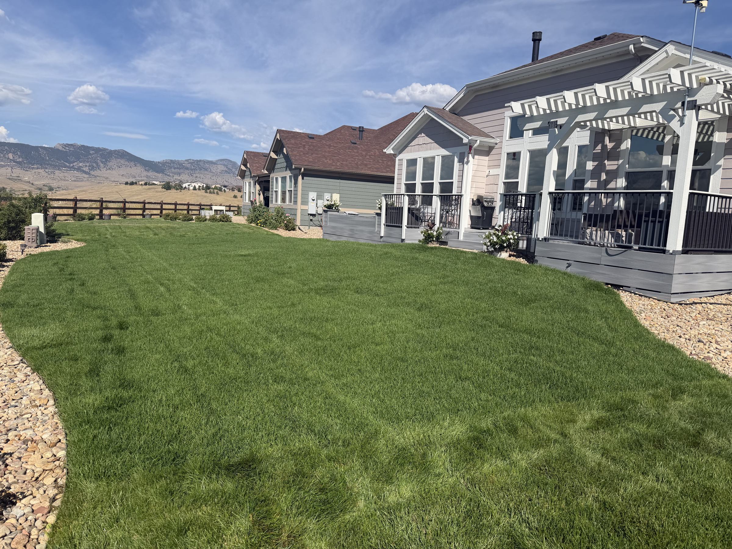 Freshly installed green sod lawn with river rock border in front of a home with a pergola and mountain views